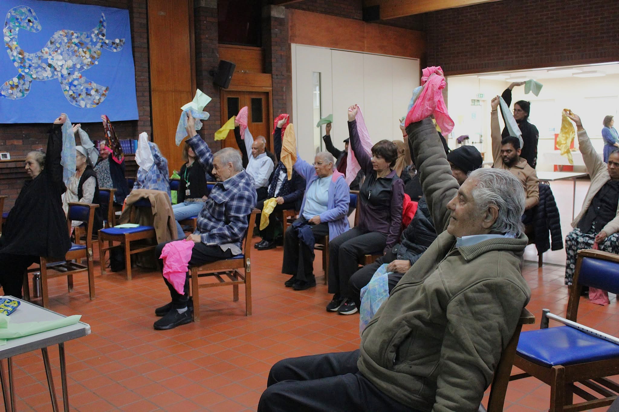 Older adults in a community hall raising colourful scarves during a dementia support workshop.